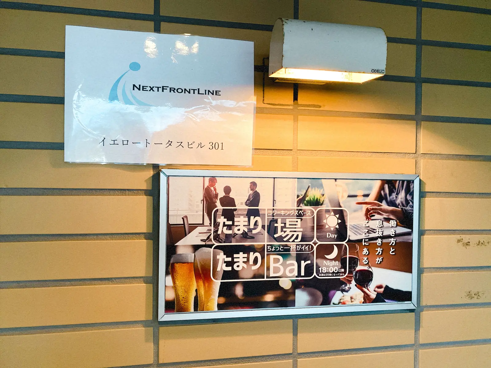 扉の横に掲示された、NextFrontLineのプレートと「たまり場／たまりBar」の看板